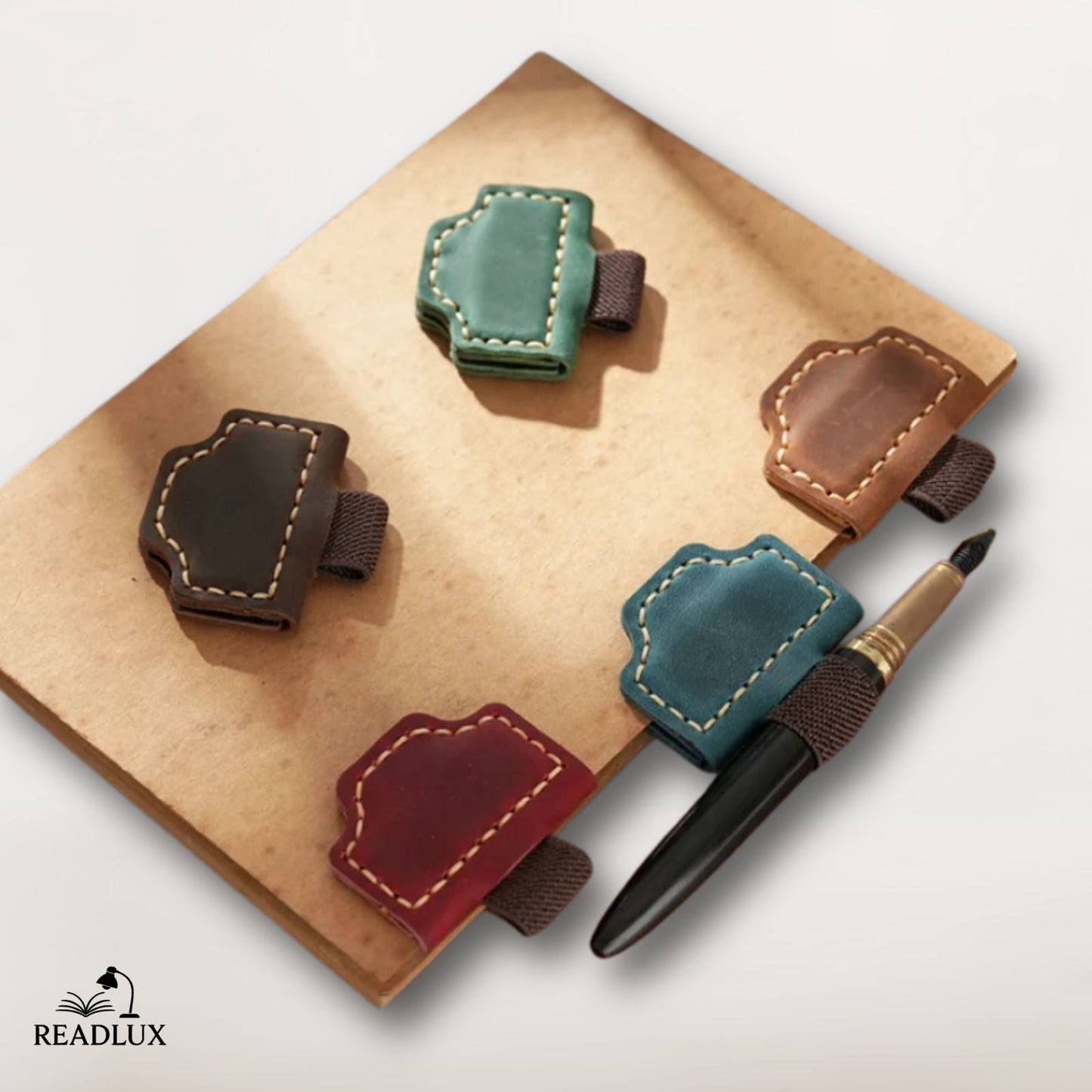 Quatre marque-pages en cuir magnétique de différentes couleurs sont posés sur un carnet en papier kraft avec un stylo noir