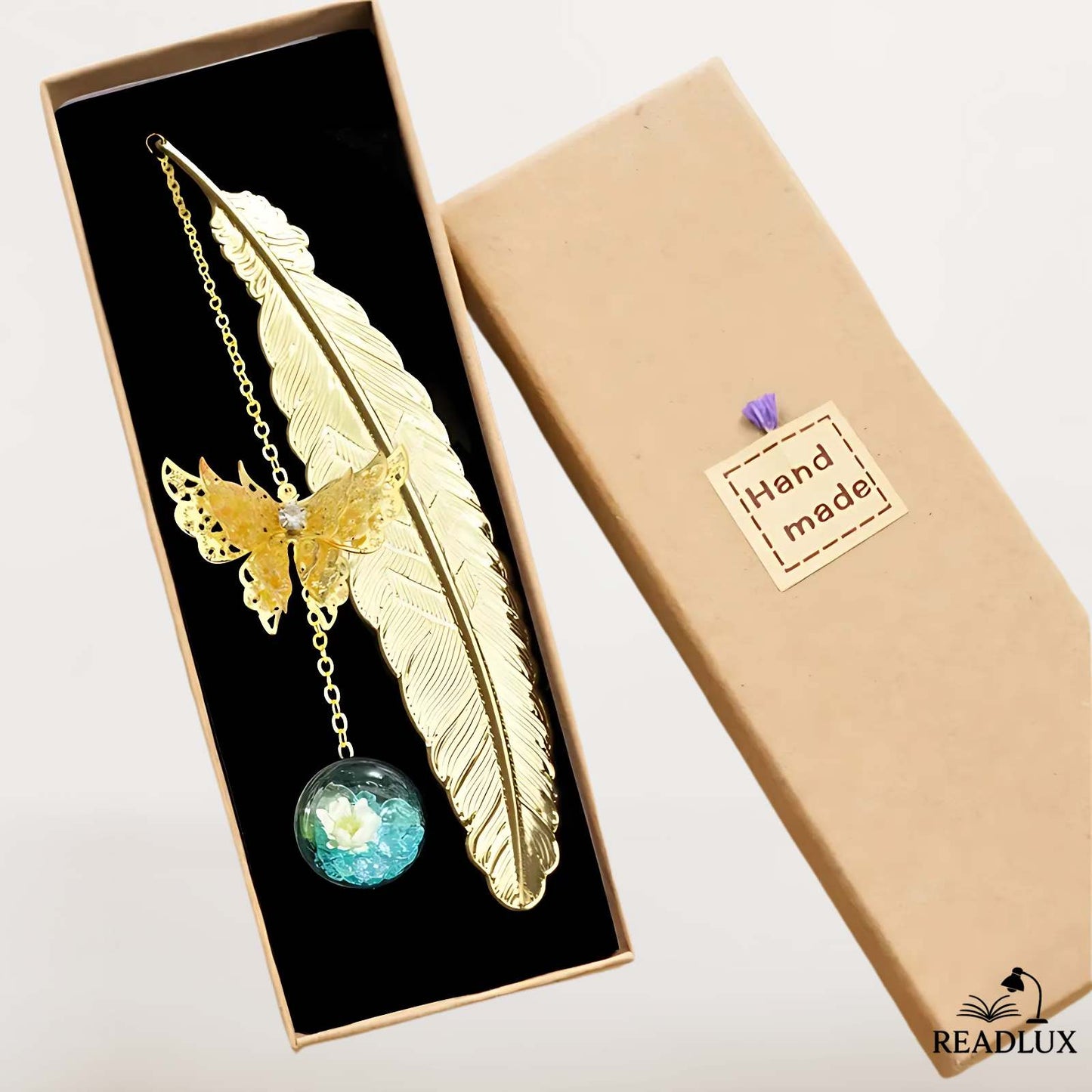 Marque page plume doré avec papillon ajouré et boule fleurie, présenté dans une boîte cadeau artisanale.