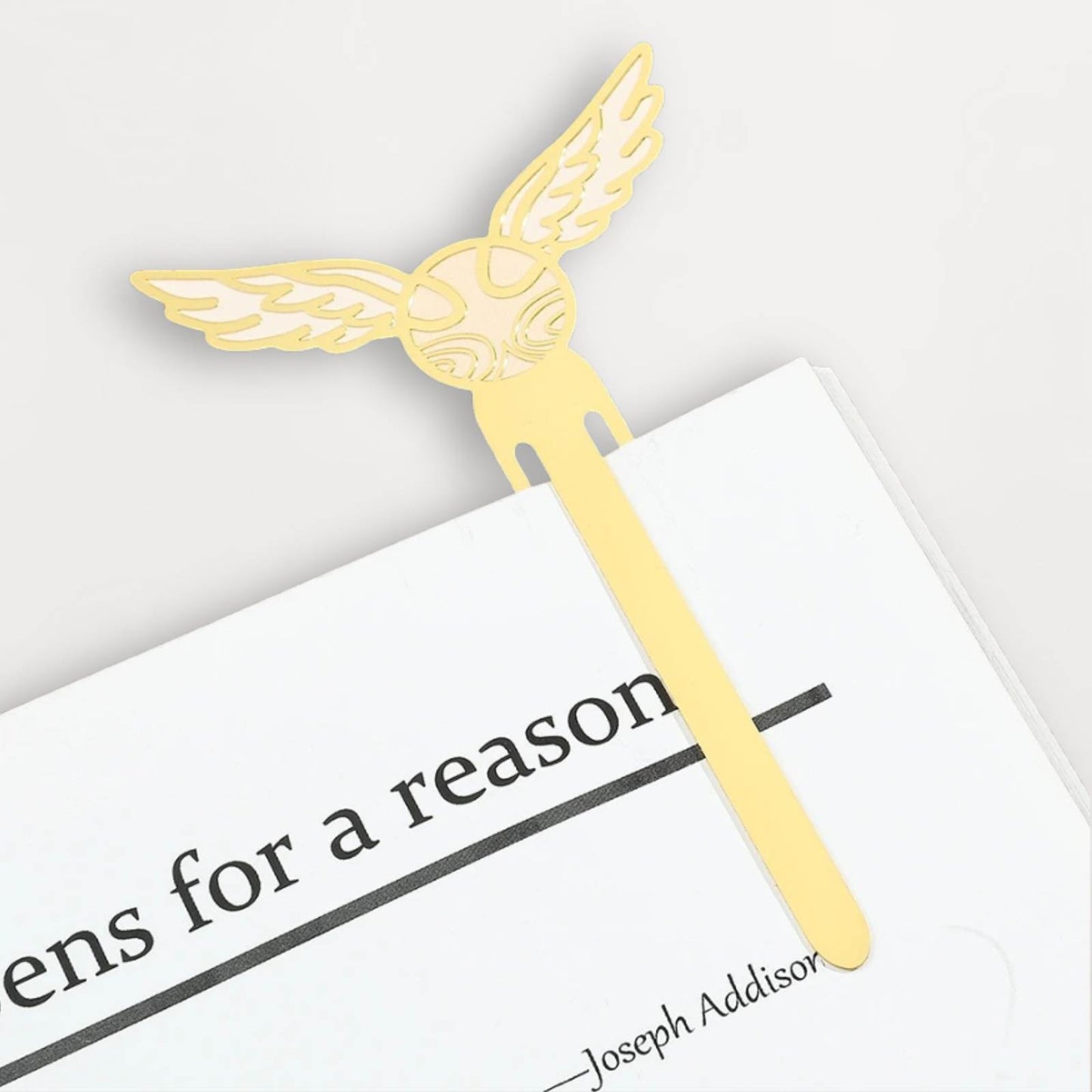 Marque-page en métal doré avec des ailes stylisées, posé sur une page blanche d'un livre