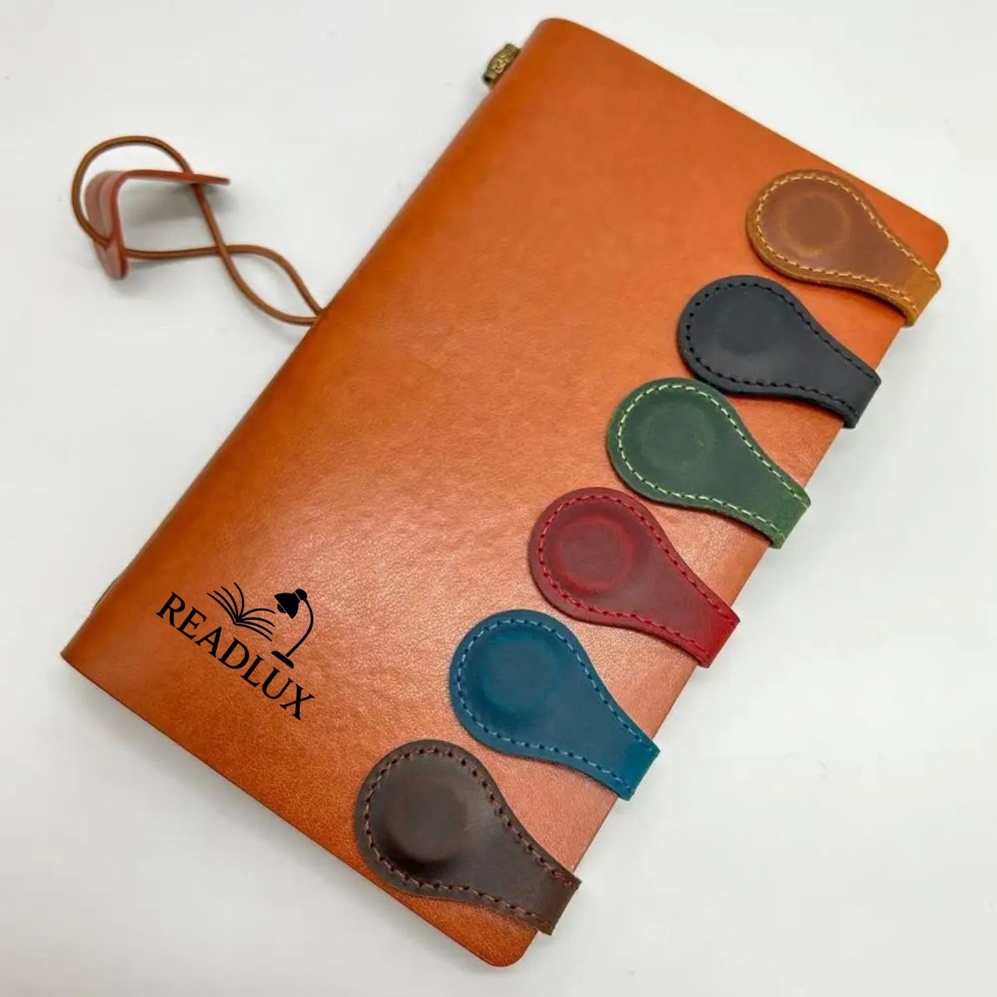 Carnet en cuir orange avec des marque-pages en cuir colorés, disposés sur le côté, sur fond blanc