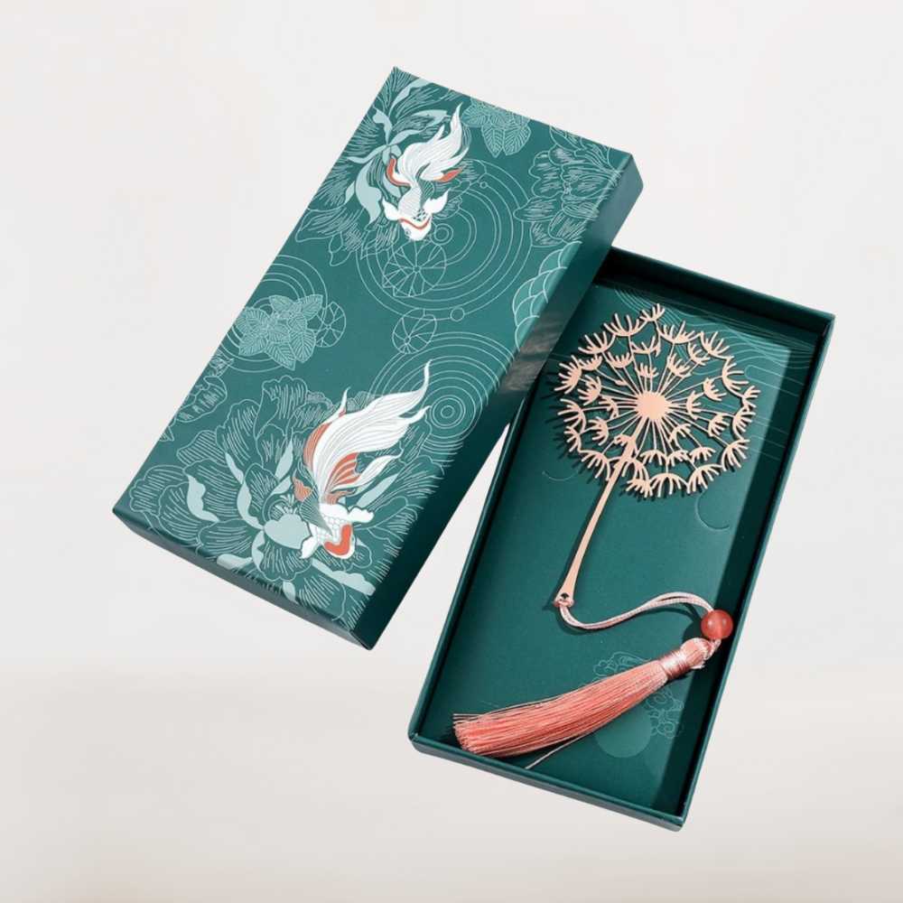 Marque page métal pissenlit rose cuivré avec pompon et perle, présenté dans une boîte cadeau illustrée élégante.