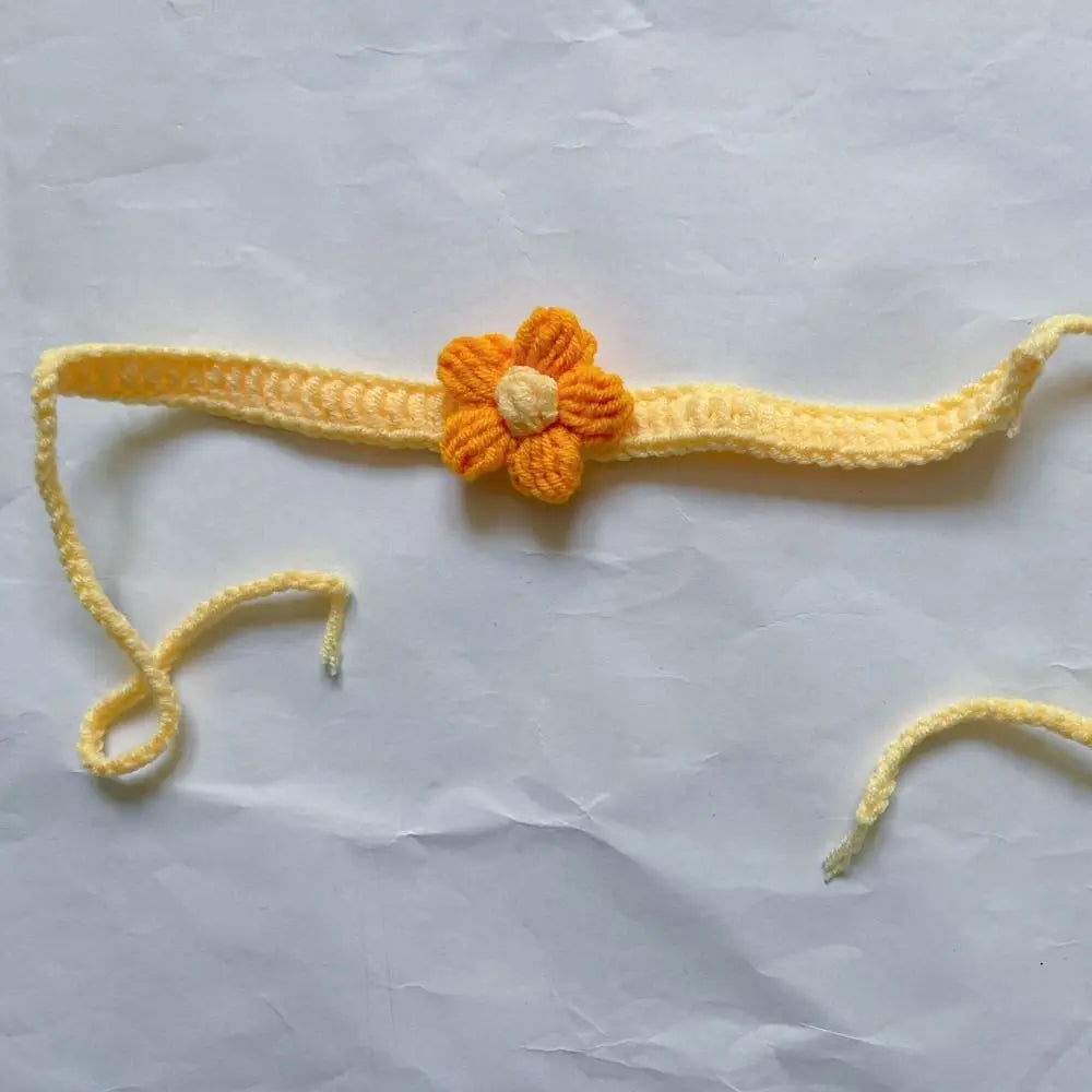 Marque-page tricoté en jaune avec une fleur orange au centre, sur fond de papier blanc froissé