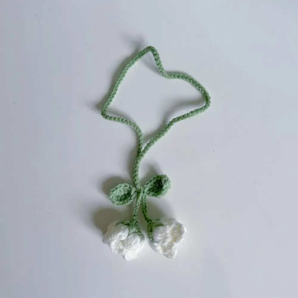 Marque-page en tricot avec deux fleurs blanches et une tige verte sur fond blanc