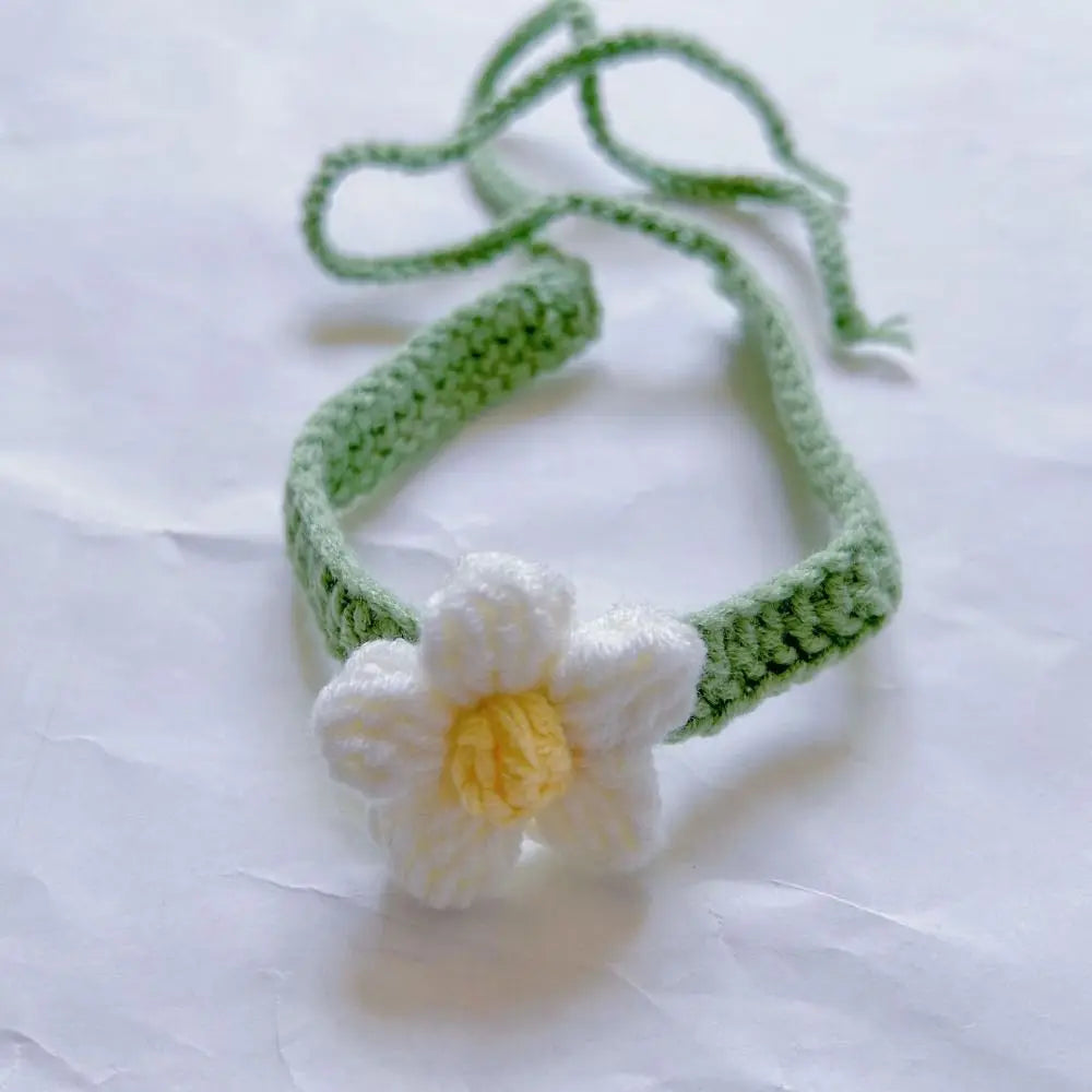 Un marque-page en tricot vert avec une fleur blanche et jaune, posé sur un fond blanc