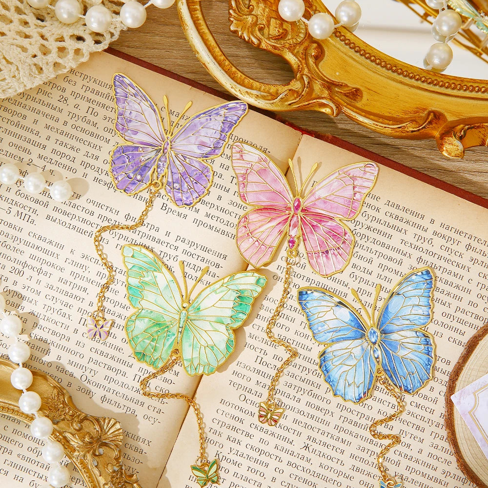 Quatre marque-pages en forme de papillon coloré, posés sur une page de livre, entourés de perles et d'un miroir doré