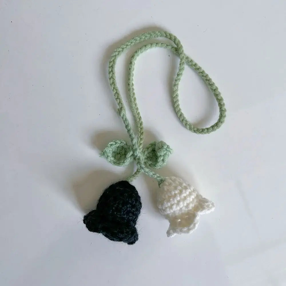 Marque-page en tricot avec une cloche noire et une cloche blanche, relié par une corde verte