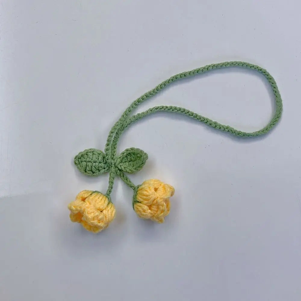 Marque-page tricoté avec deux fleurs jaunes et des feuilles vertes sur un fond gris clair
