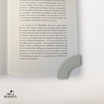 Marque-page en cuir gris en forme de cœur, posé sur une page d'un livre ouvert, décor sobre et élégant