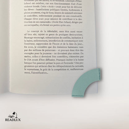 Un marque-page en cuir vert clair, en forme de cœur, posé sur une page d'un livre ouvert