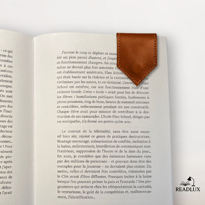 Un marque-page en cuir marron, en forme de flèche, posé sur une page d'un livre ouvert