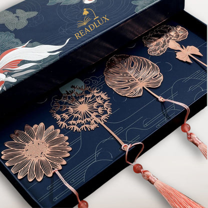 Quatre marque-pages en métal rose doré, présentés sur un fond bleu décoré de motifs aquatiques