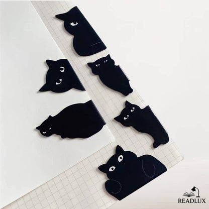 Marque pages magnétiques noirs en forme de chats, posés sur carnet à pages blanches et quadrillées.