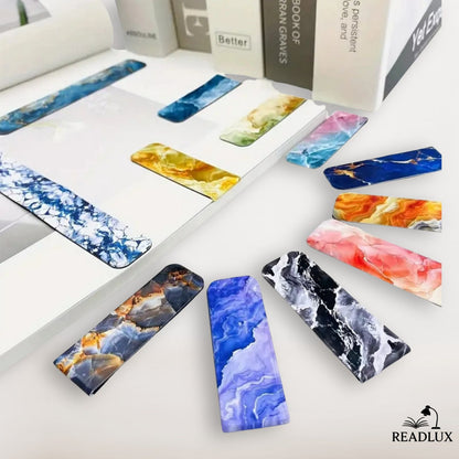 Lot de marque pages magnétiques avec motifs effet marbre coloré, dégradés de bleu, orange, rose, violet et doré présentés dans un livre.