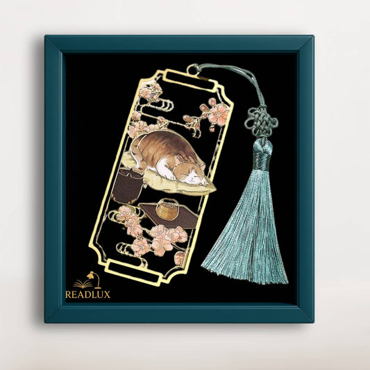 Marque page en métal doré avec chat roux endormi, fleurs de cerisier et pompon vert raffiné.