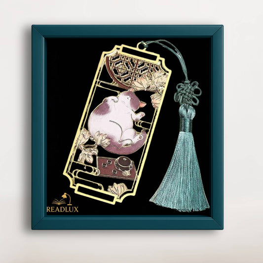 Marque page en métal doré avec chat blanc endormi, fleurs ajourées et pompon vert élégant.