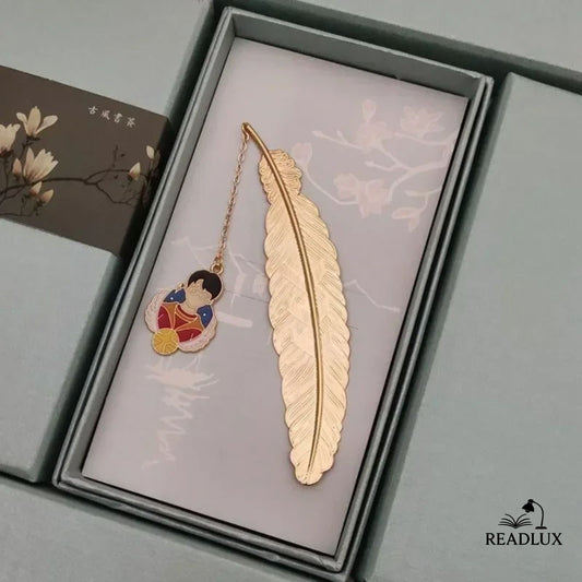 Marque page plume dorée en métal avec pendentif illustré d’un jeune sorcier en rouge, style enchanté et narratif