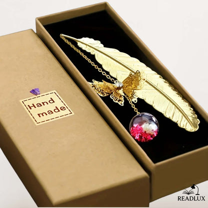 Marque page plume dorée en métal avec pendentif floral, présenté dans un écrin élégant