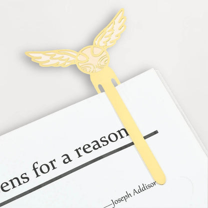 Marque-page en métal doré avec des ailes stylisées, posé sur une page blanche d'un livre