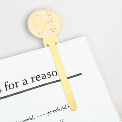 Marque-page en métal doré avec le numéro 9¾, posé sur une page blanche d'un livre ouvert