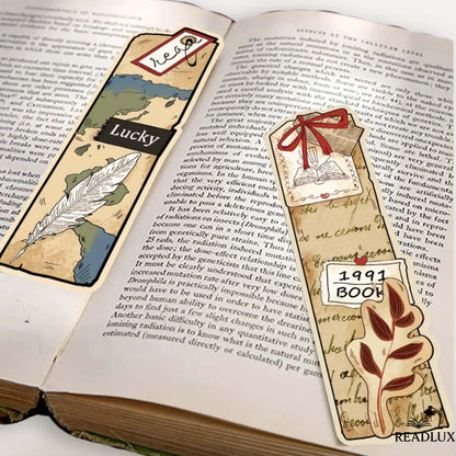 Deux marque-pages vintage en papier sur une page de livre, avec des motifs de carte et de plumes