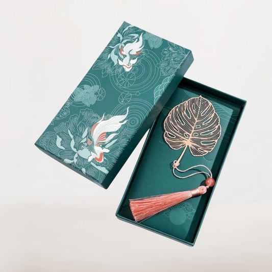 Marque page en métal rose doré en forme de feuille tropicale avec pompon, présenté dans un coffret vert Readlux