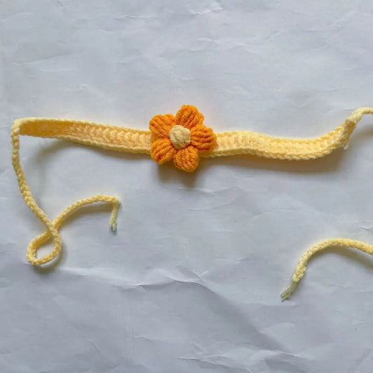 Marque-page tricoté en jaune avec une fleur orange au centre, sur fond de papier blanc froissé