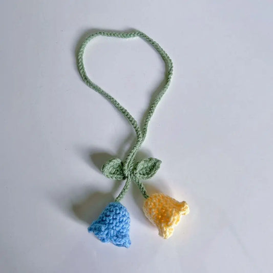 Marque-page en tricot avec deux fleurs en bleu et jaune, attachées par une tige verte sur fond blanc
