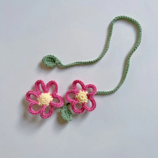 Marque-page en tricot avec deux fleurs roses et jaunes, attachées par une tige verte, sur fond blanc