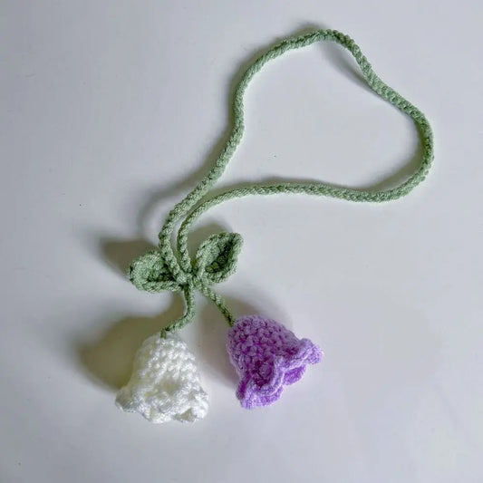 Marque-page tricoté en forme de fleurs blanches et violettes avec une tige verte sur fond blanc