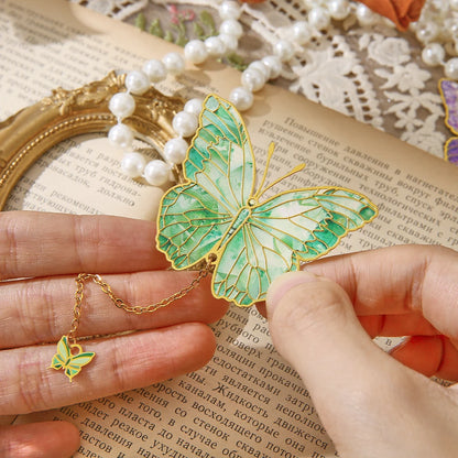 Un marque-page en métal en forme de papillon vert, délicatement tenu entre des doigts sur une page de livre