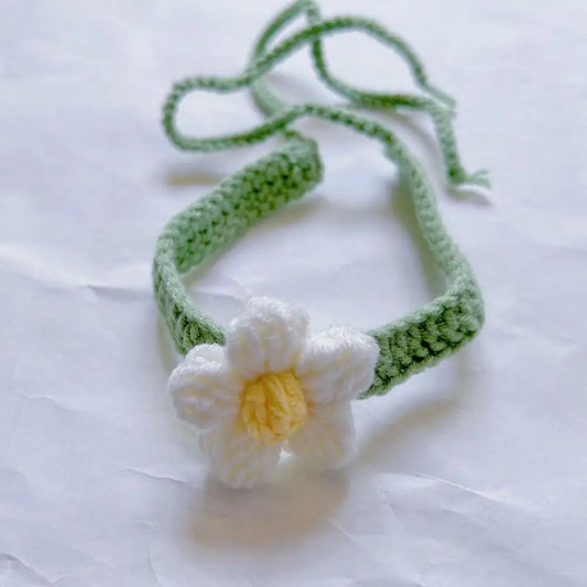 Un marque-page en tricot vert avec une fleur blanche et jaune, posé sur un fond blanc