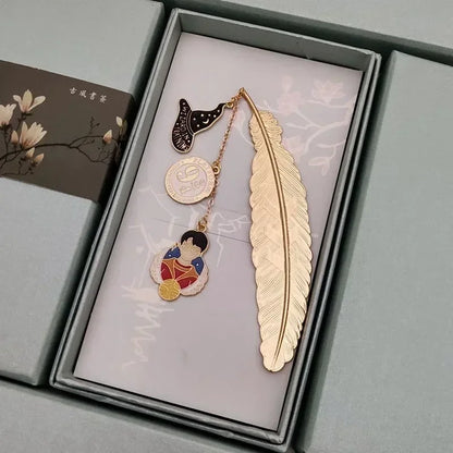 Un marque-page en métal doré en forme de plume, avec des pendentifs colorés sur un fond clair