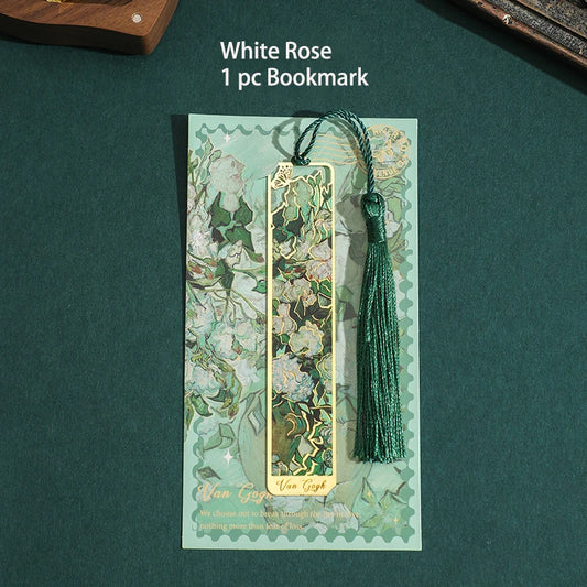 Marque-page en métal doré avec motif floral vert et blanc, accompagné d'un pompon vert sur fond sombre