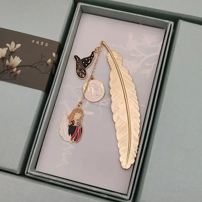 Un marque-page en métal doré en forme de plume avec des pendentifs colorés sur un fond bleu clair