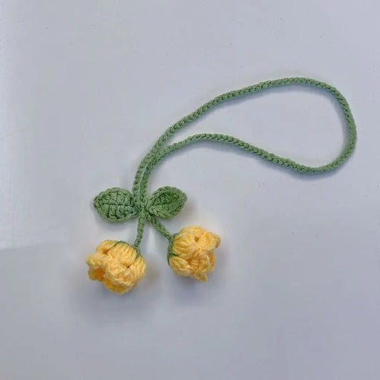 Marque-page tricoté avec deux fleurs jaunes et des feuilles vertes sur un fond gris clair