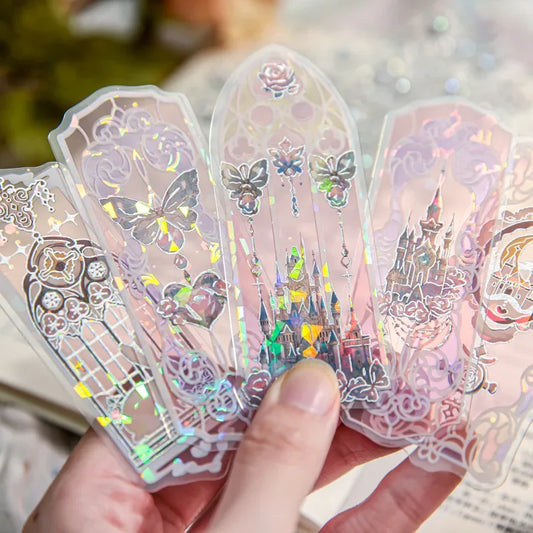 Marque-pages en PVC translucide avec motifs holographiques, représentant des châteaux et des fleurs, tenus dans une main