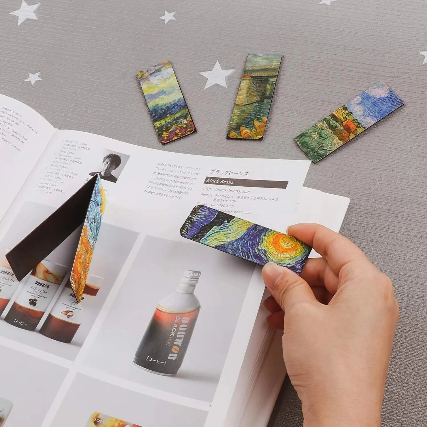 Quatre marque-pages magnétiques colorés avec motifs artistiques, posés sur une page d'un livre ouvert sur un fond gris