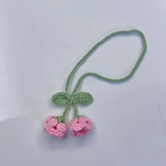 Marque-page en tricot avec deux fleurs roses et des feuilles vertes, sur fond blanc