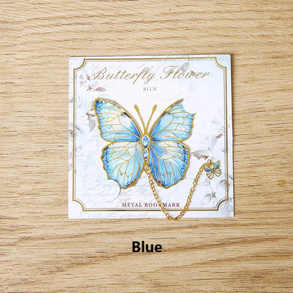 Un marque-page en métal représentant un papillon bleu avec des détails dorés sur un fond décoratif floral