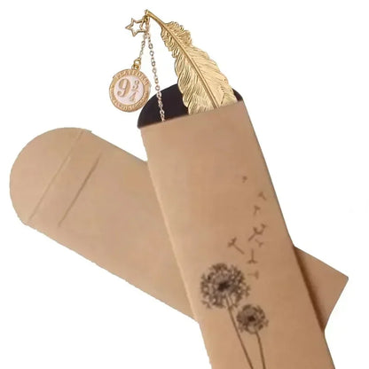 Un marque-page doré en forme de plume, suspendu dans une enveloppe en papier kraft décorée de pissenlits