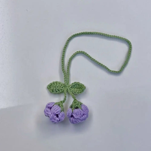 Marque-page en tricot avec deux fleurs violettes et des feuilles vertes sur fond blanc