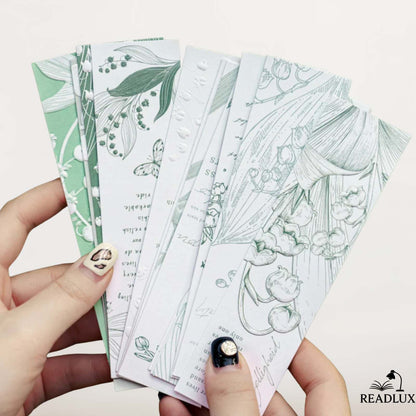 Des marque-pages en papier illustrés de motifs floraux délicats dans des tons verts et blancs, tenus par une main