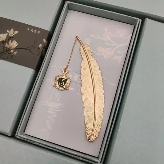 Marque page plume dorée en métal avec insigne noir suspendu, style sorcier élégant, mystérieux et symbolique